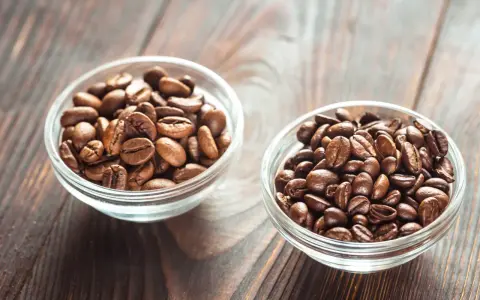 Dwie miseczki z ziarnami kawy: jaśniejsza arabika i ciemniejsza robusta, na drewnianym tle.