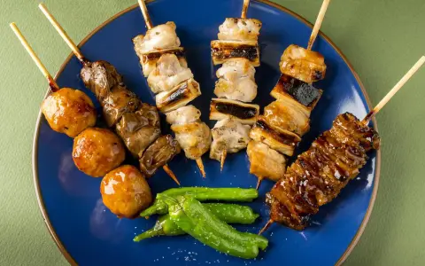 Różnorodne yakitori na niebieskim talerzu: kurczak, wątróbka, klopsiki i papryczki shishito.