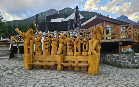Drewniane rzeźby niedźwiedzi tworzą napis HREBENOK. W tle budynek z tarasem i góry. Sprawdź hrebienok kolejka cennik.