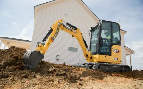 Żółta koparka gąsienicowa Caterpillar 302 CR pracuje na budowie domu, kopiąc ziemię.