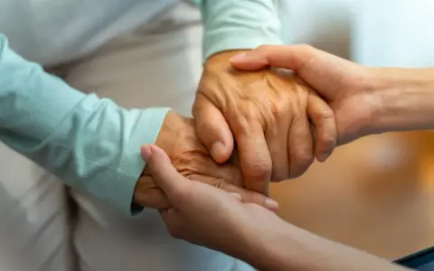 Dwie dłonie, starsza i młodsza, splatają się w geście wsparcia. Zastanawiasz się, komu przysługuje zasiłek za opiekę nad osobą starszą?