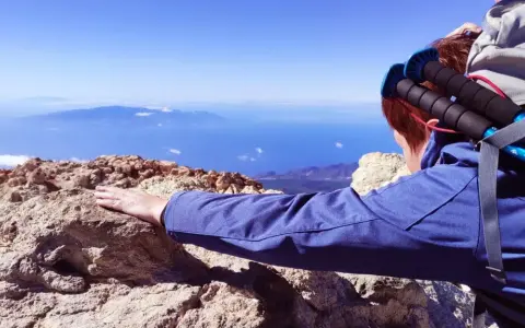 Blick vom Gipfel nach der Teide Wanderung. Ein Wanderer lehnt sich auf Felsen, mit Blick auf das weite Meer und ferne Inseln.
