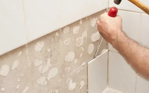 Main d'un bricoleur en pleine action pour enlever carrelage mural avec un burin et un marteau. La surface est prête pour un nouveau revêtement.
