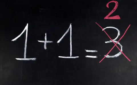 Na czarnej tablicy napisano kredą: 1+1=3. Dwójka jest podkreślona na czerwono, a trójka przekreślona. Jak na egzaminie dojrzałości, gdzie liczy się poprawna odpowiedź.