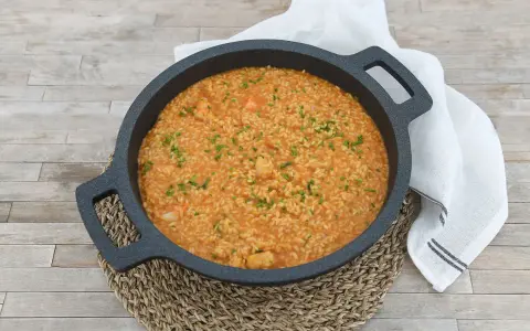Arroz cremoso con gambones, adornado con cebollino fresco, servido en una paellera sobre una mesa de madera.