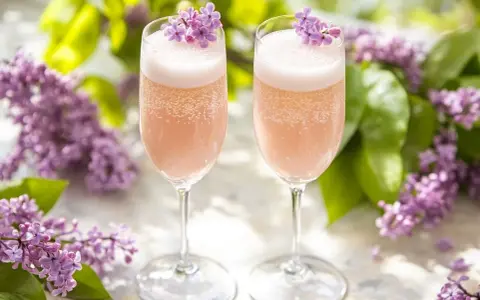 Två glas med rosa bubbel, dekorerade med syrenblommor. Perfekt för ett syrensirap recept.
