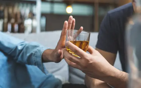 Dłoń odrzuca szklankę z alkoholem. Przykład asertywnego odmawiania picia alkoholu.