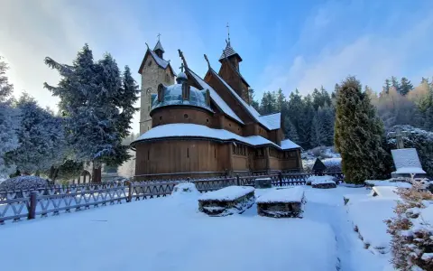 Drewniana świątynia Wang w Karkonoszach, otoczona ośnieżonymi drzewami i cmentarzem, wygląda magicznie w zimowym słońcu.