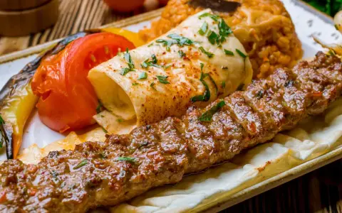 Kebab z mięsa mielonego, grillowane warzywa, placek i ryż na talerzu.