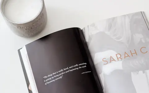 Otwarta książka z cytatem o tym, jak znaleźć swój styl, obok świecy. Na stronie widnieje napis "SARAH C".