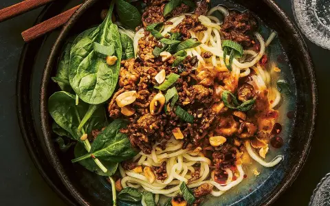 En skål med dan dan nudlar, toppad med köttfärs, jordnötter och sallad.