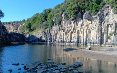 Un'oasi naturale nella Tuscia: un fiume serpeggia tra imponenti pareti rocciose ricoperte di vegetazione, creando uno scenario suggestivo.
