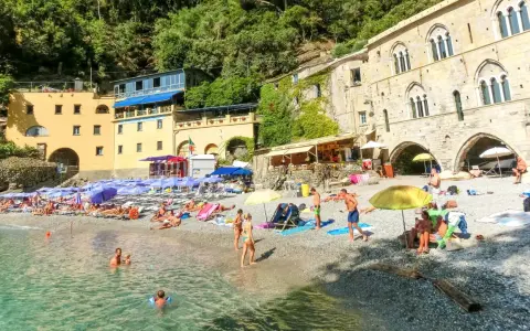 Ein idyllischer **Geheimtipp Italien Strand** mit bunten Sonnenschirmen, sonnenbadenden Menschen und kristallklarem Wasser vor malerischer Kulisse.