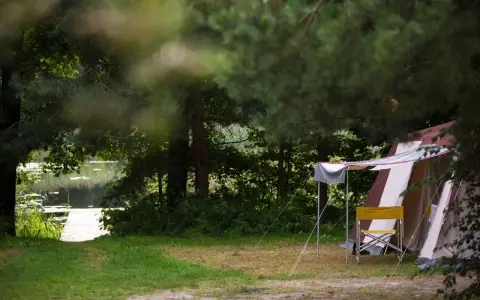 Namiot i krzesło na tle jeziora i lasu. Idealne pola namiotowe Mazury dla miłośników natury.