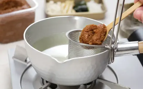 Łyżka z pastą miso trafia do bulionu. Tak przygotowuje się bazę do zupy, pytasz miso co to? To fermentowana pasta sojowa.