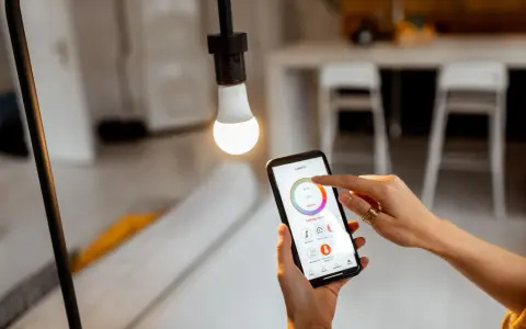 Mano ajustando el control de iluminacion domotica en un smartphone para regular la luz de una bombilla.