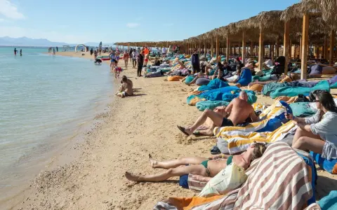Słoneczna plaża w Egipcie w maju. Ludzie odpoczywają na leżakach pod palmowymi parasolami, ciesząc się piękną pogodą.