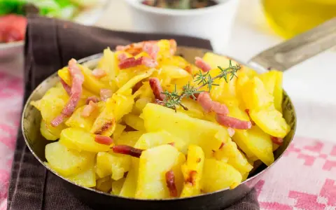 Patatas al microondas con trocitos de bacon crujiente y romero fresco, servidas en una sartén metálica. ¡Un plato rápido y delicioso!