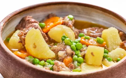 Un reconfortante ragout de ternera con patatas, zanahorias y guisantes en un cuenco rústico.