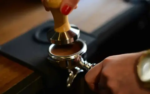 Barista tamped den gemahlenen Kaffee für einen perfekten Espresso. Die Espresso-Definition beginnt hier.