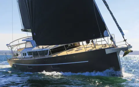 Un voilier moderne, avec une grande voile noire, navigue sur une mer agitée. Xavier Desmarest admire la vue depuis le pont.