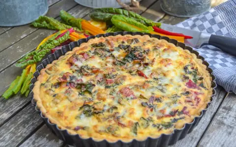 Herzhaftes Mangold Quiche Rezept, frisch gebacken und bereit zum Genießen. Bunte Mangoldstiele liegen daneben.