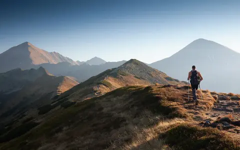 Wędrowiec na grani Tatr, odkrywa malownicze tatry szlaki dla średnio zaawansowanych. Słońce oświetla zbocza.