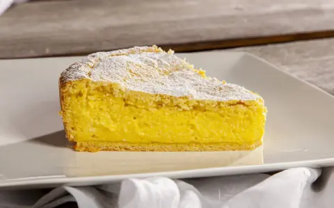Una fetta di crostata di ricotta, con la sua base dorata e il ripieno cremoso, spolverata di zucchero a velo.