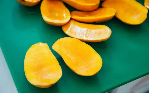Pokrojone w łódeczki, soczyste mango w intensywnym kolorze, jakby w ciąży z owocową obfitością, leżą na zielonej desce.