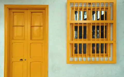 Une porte et une fenêtre avec un encadrement de porte couleur différente, le tout peint en jaune vif sur un mur blanc texturé.