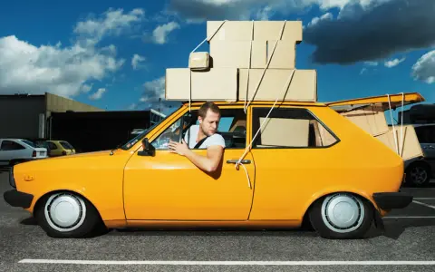 Hombre en coche amarillo cargado de cajas, preguntándose cuanto peso aguanta un coche.