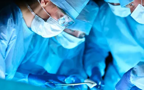 Chirurdzy w niebieskich fartuchach i maskach operacyjnych podczas zabiegu.