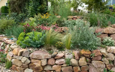 Ein wunderschöner Steingarten, der zeigt, wie man mit wenig Geld einen tollen Garten gestalten kann. Bunte Blumen und Gräser wachsen zwischen Natursteinen.