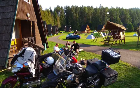 Motocykliści odpoczywają na kempingu w Rumunii, otoczeni drewnianymi domkami i lasem.