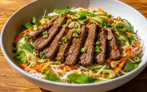 En skål med asiatisk biffsallad med nudlar, strimlad biff, gurka, morötter, mynta och jordnötter.