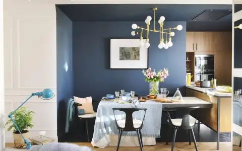 El azul oscuro combina con tonos pastel, madera y dorado. Un comedor elegante con mesa, sillas negras, lámpara dorada y flores.