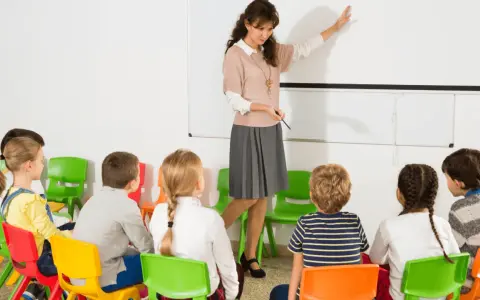 Nauczycielka prowadzi lekcję dla dzieci w klasie. To początek roku szkolnego w Hiszpanii, dzieci siedzą na kolorowych krzesełkach.