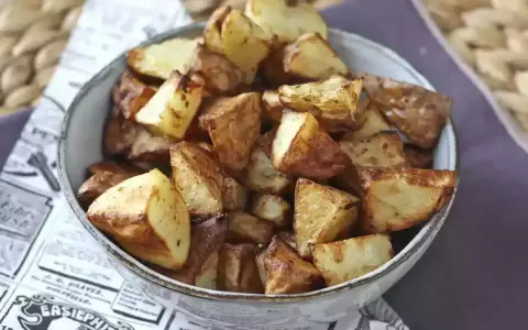 Patate dorate e croccanti in friggitrice ad aria, servite in una ciotola su carta di giornale.