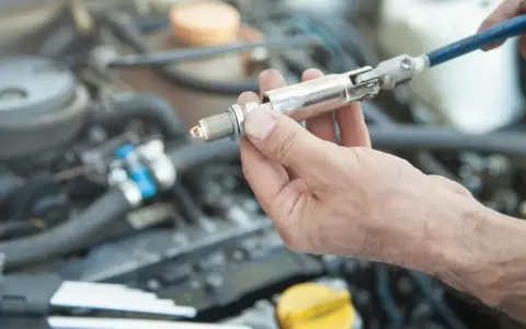 A hand holds a spark plug with a socket wrench attached, ready for a spark plug replacement. This DIY task can save on the spark plug replacement cost.