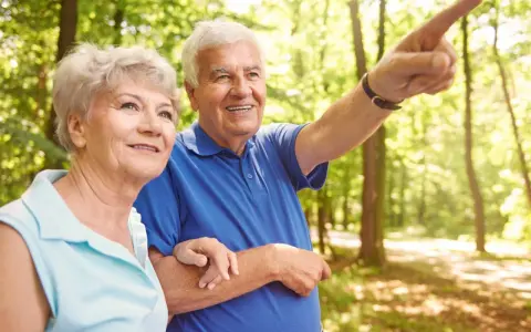 Uśmiechnięty senior od jakiego wieku? Wskazuje drogę podczas spaceru po lesie z ukochaną.