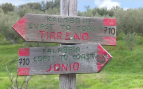 Cartelli in legno indicano il percorso "Kalabria Coast to Coast": uno punta a Tirreno, l'altro a Jonio.