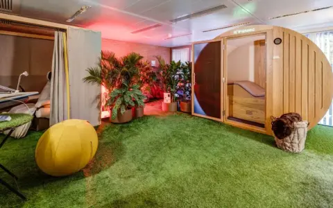 Une salle de pause originale avec un gazon synthétique, une cabine en bois, des plantes et un fauteuil de massage.