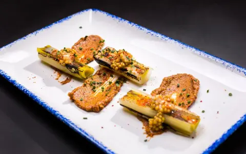 Puerros a baja temperatura, tiernos y dorados, servidos con una sabrosa salsa y granos de mostaza.