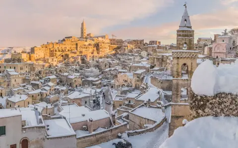 Matera innevato, un incanto tra i **posti da visitare in inverno Italia**. Case antiche e chiese sotto la neve, con il sole che illumina il paesaggio.