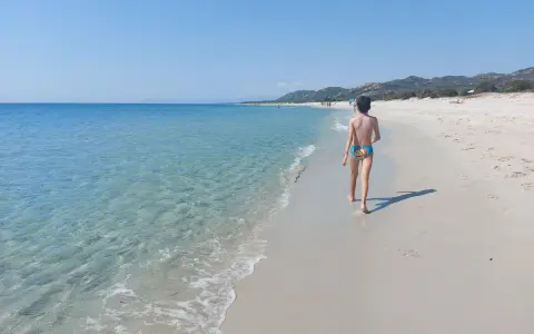 Un bambino cammina su una spiaggia di sabbia bianca, verso le spiagge più belle della Sardegna est. Acqua cristallina e cielo azzurro.