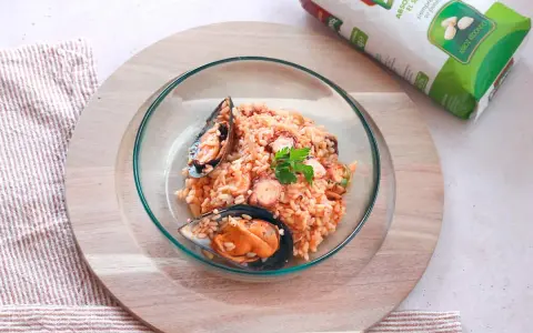 Delicioso arroz con pulpo y mejillones, servido en un cuenco de cristal sobre una tabla de madera.