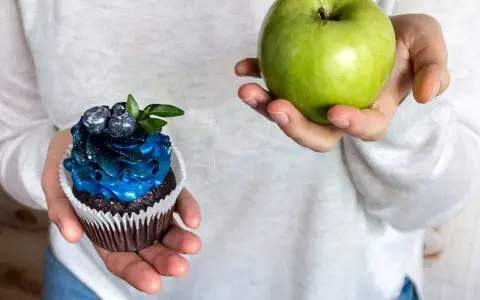 En hand håller ett grönt äpple, den andra en dekorerad cupcake. Ett val för en socker detox.