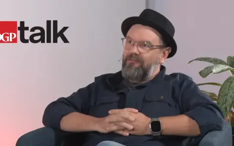 Mężczyzna w okularach i kapeluszu siedzi, rozmawiając. Obok logo DGP talk.
