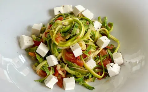 Spaghetti di zucchine freschi con pomodoro e cubetti di feta, conditi con pepe nero.