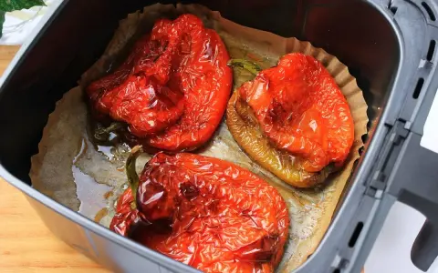 Tres pimientos rojos asados en freidora de aire, con la piel arrugada y jugosos, listos para disfrutar.